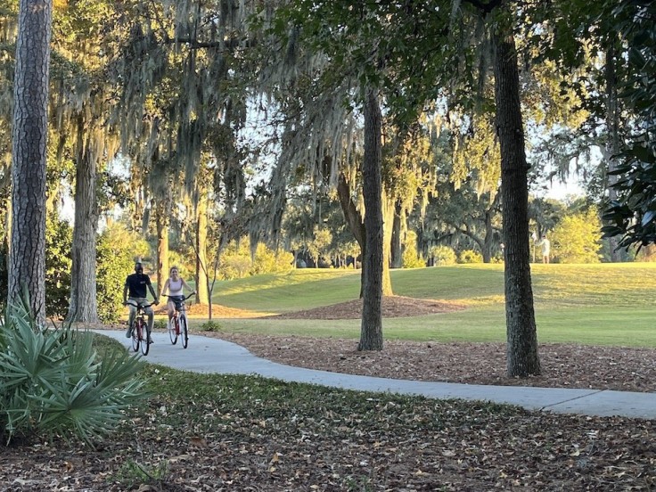 man and woman biking on path next to golf course under trees