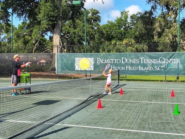little girl practicing tennis with instructor on court