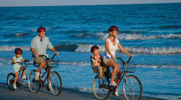 Family of four biking on tandem bikes along beach