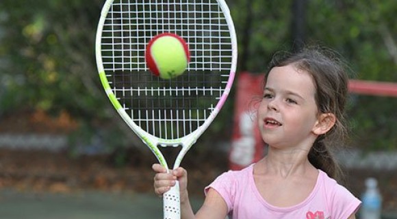 Close up of a young girl hitting a tennis ball outside