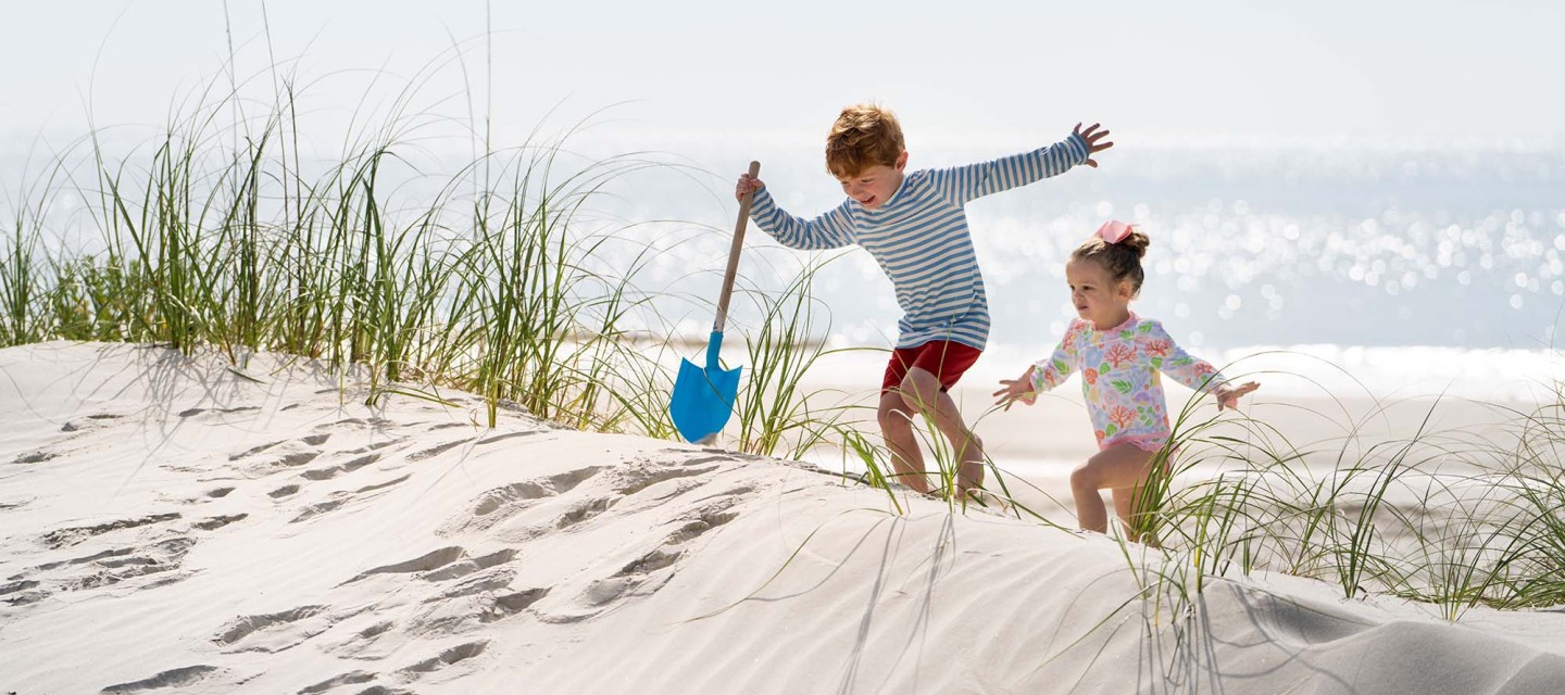 two children climbing up a dune with blue shovel in hand at Hilton Head Island Beach