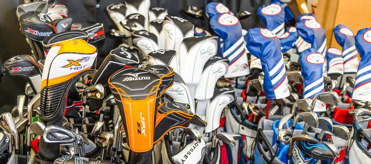 Closeup of several rows of golf backs with clubs inside of them.