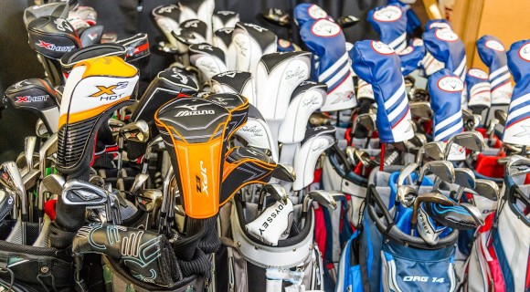 Closeup of several rows of golf backs with clubs inside of them.